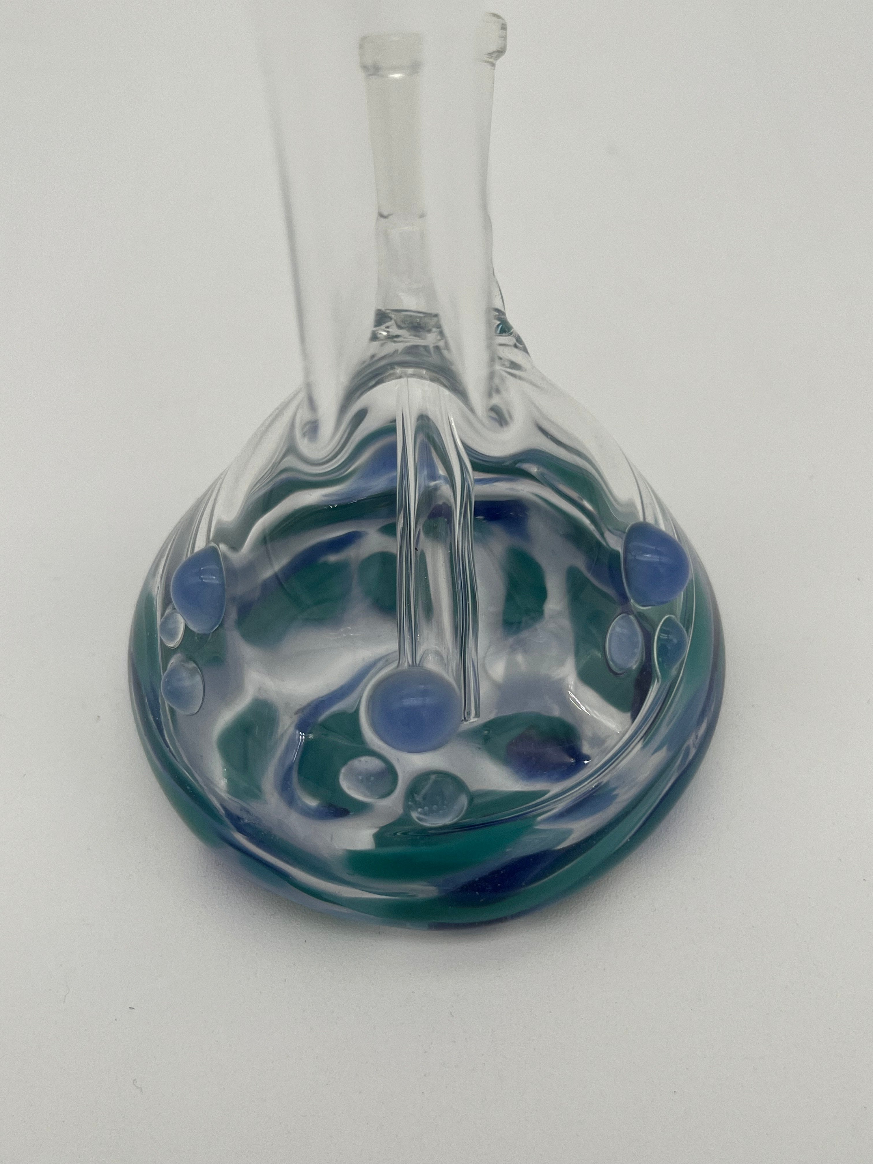 Handblown glass beaker mini bong. 10mm downstem. Made by CGlass and Dan Ottone. Clear beaker with blue and green details on a white background.