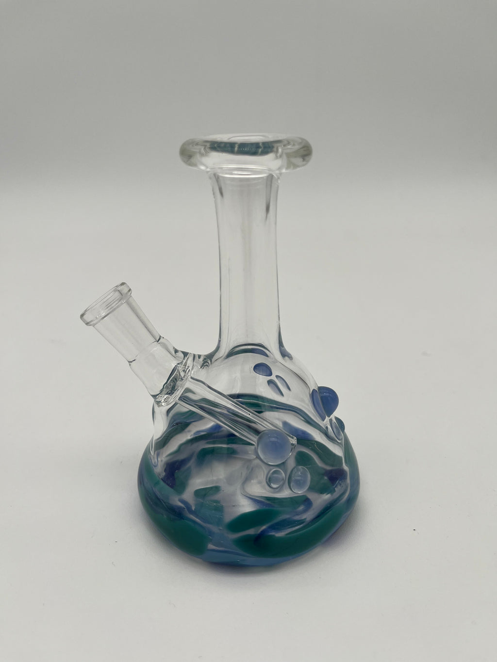 Handblown glass beaker mini bong. 10mm downstem. Made by CGlass and Dan Ottone. Clear beaker with blue and green details on a white background.
